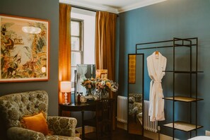 A room with a patterned armchair, a mirror, a robe rack, and a floral arrangement.