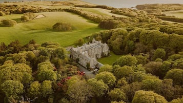 A large, historic building surrounded by lush greenery and rolling hills.