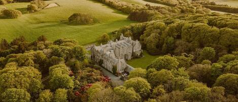 A large, historic building surrounded by lush greenery and rolling hills.