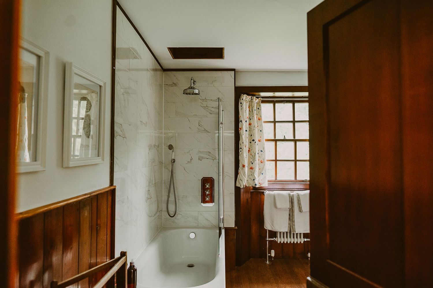 Een badkamer met een douche, een raam met gordijnen, en een houten vloer.