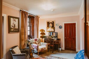 A room with a chair, a table, a mirror, a door, and a framed picture on the wall.