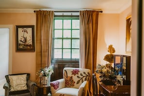 A room with a window, a chair, a table, and a vase with flowers.