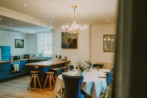 A modern kitchen with a central island, a dining area with a round table and blue chairs, and a chandelier.