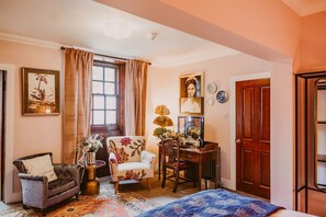 A cozy room with a bed, a chair, a desk, and a window with curtains.