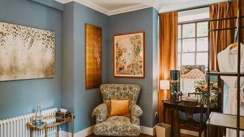 A room with a patterned armchair, a radiator, a table with a lamp, and a bed with a headboard.
