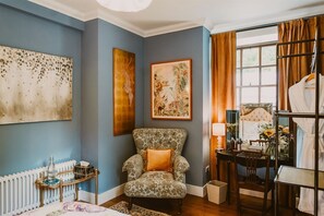 Habitació amb una butaca estampada, un radiador, una taula amb una làmpada i un llit amb capçalera.