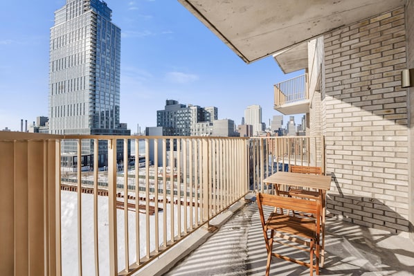 A balcony with a wooden table and chairs, overlooking a cityscape with modern buildings. - The Quay Waypost Hospitality Greenpoint (brooklyn)