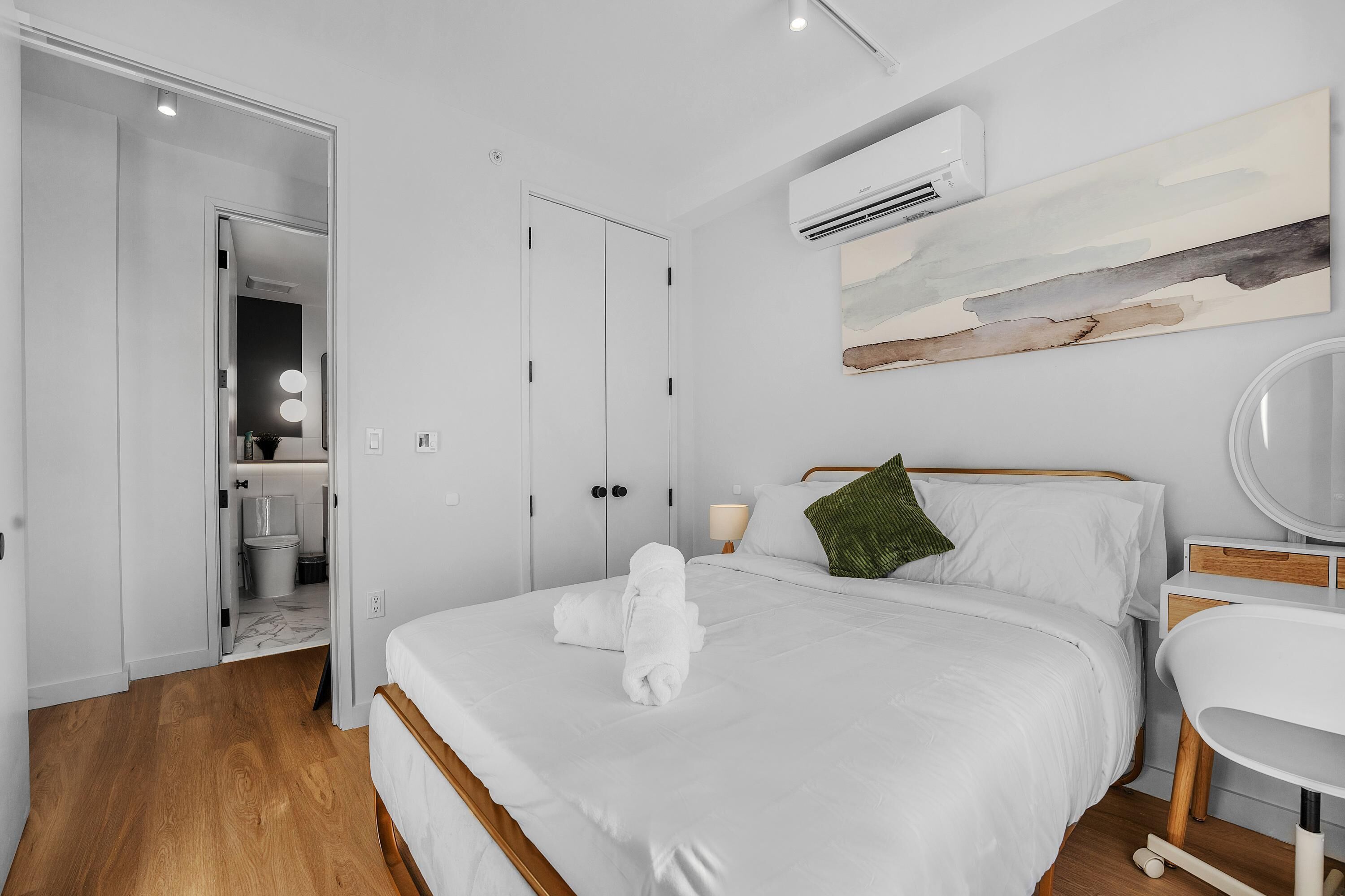 A hotel room with a bed, a bedside table, a mirror, and an air conditioning unit.