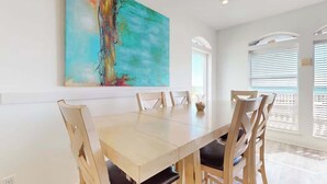 Un coin repas avec une grande table, six chaises et un tableau abstrait aux couleurs vives accroché au mur.
