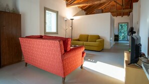 A room with a red patterned sofa, a yellow sofa, a wooden cabinet, a television, and a ceiling with exposed beams. - GuestHost - Lisignano Cozy Apartment with Parking (Gazzola)