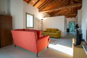 Ein Zimmer mit einem roten, gemusterten Sofa, einem gelben Sofa, einem Holzschrank, einem Fernseher und einer Decke mit freiliegenden Balken.
