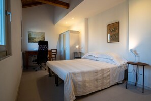 Un dormitorio con cama, escritorio y silla, armario y mesita de noche con lámpara.