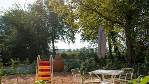 A garden with a table and chairs, a swing set, and a large pot. - GuestHost - Lisignano Cozy Apartment with Parking (Gazzola)