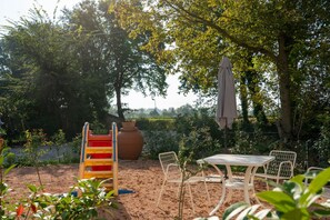 A garden with a table and chairs, a swing set, and a large pot.