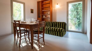 A dining area with a wooden table and chairs, a striped sofa, and a built-in bookshelf. - GuestHost - Lisignano Cozy Apartment with Parking (Gazzola)