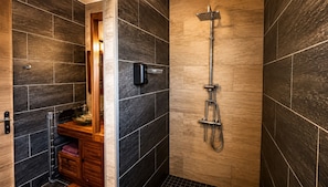 Ein modernes Badezimmer mit dunklen Fliesen, einem Holz-Waschtisch und einer Duschkabine aus Glas mit Handbrause.