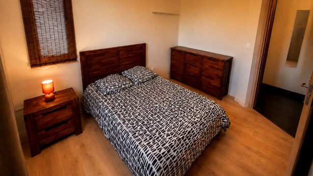 Une chambre à coucher avec un lit en bois, une table de chevet avec une lampe, une armoire et un luminaire suspendu.
