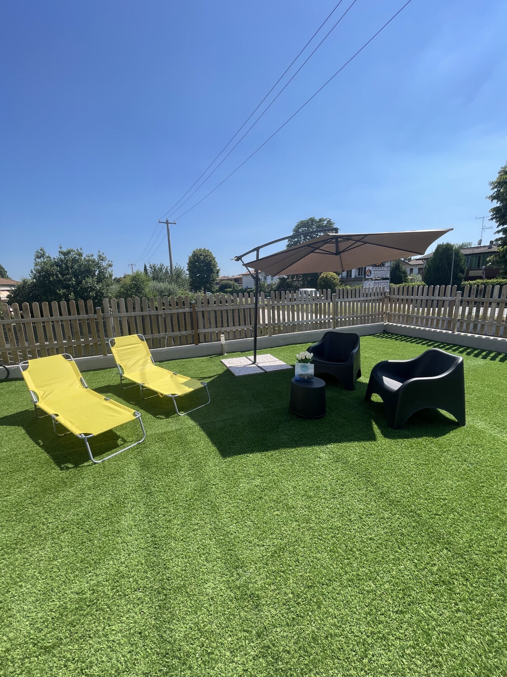 Un espacio al aire libre con césped artificial, sillones reclinables amarillo y negro, y una sombrilla.