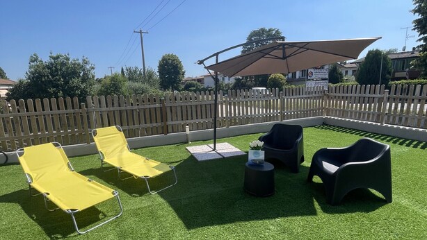 An outdoor seating area with artificial grass, yellow and black lounge chairs, and a shaded umbrella. - Garda Hub Retreat by Booking Garda Lake (Puegnago sul Garda)
