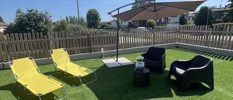 Un espacio al aire libre con césped artificial, sillones reclinables amarillo y negro, y una sombrilla.