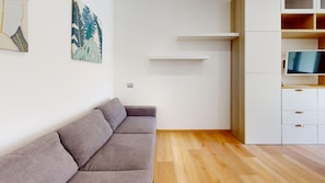 Ein modernes Wohnzimmer mit grauem Sofa, Holzboden, einem Fernseher auf einer Holzkommode und Wandregalen.