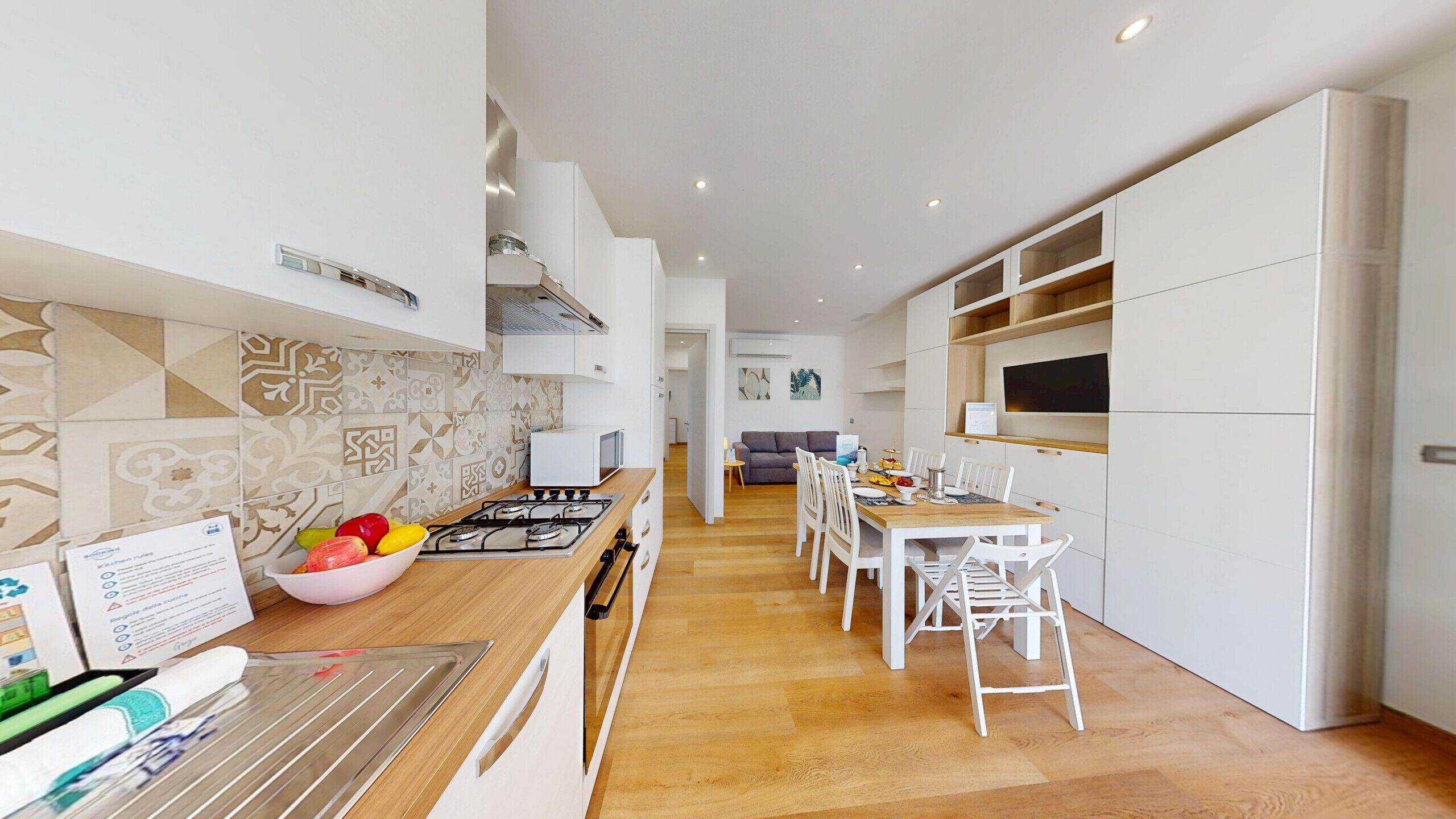 A modern kitchen with a central island, white cabinetry, and a dining area with a wooden table and white chairs.