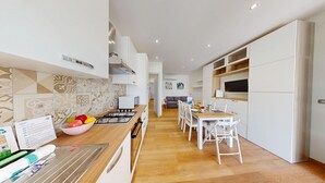 A modern kitchen with a central island, white cabinetry, and a dining area with a wooden table and white chairs. - Garda Hub Retreat by Booking Garda Lake (Puegnago sul Garda)