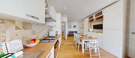 A modern kitchen with a central island, white cabinetry, and a dining area with a wooden table and white chairs.