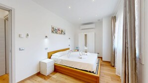 A bedroom with a wooden bed, white bedding, a bedside table, a wall-mounted air conditioner, and a door with a mirror. - Garda Hub Retreat by Booking Garda Lake (Puegnago sul Garda)