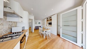 A modern kitchen with a gas stove, white cabinets, and a dining area with a table and chairs. - Garda Hub Retreat by Booking Garda Lake (Puegnago sul Garda)
