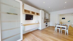 Una cocina moderna con electrodomésticos integrados, un comedor con mesa y sillas, y un televisor montado en la pared.