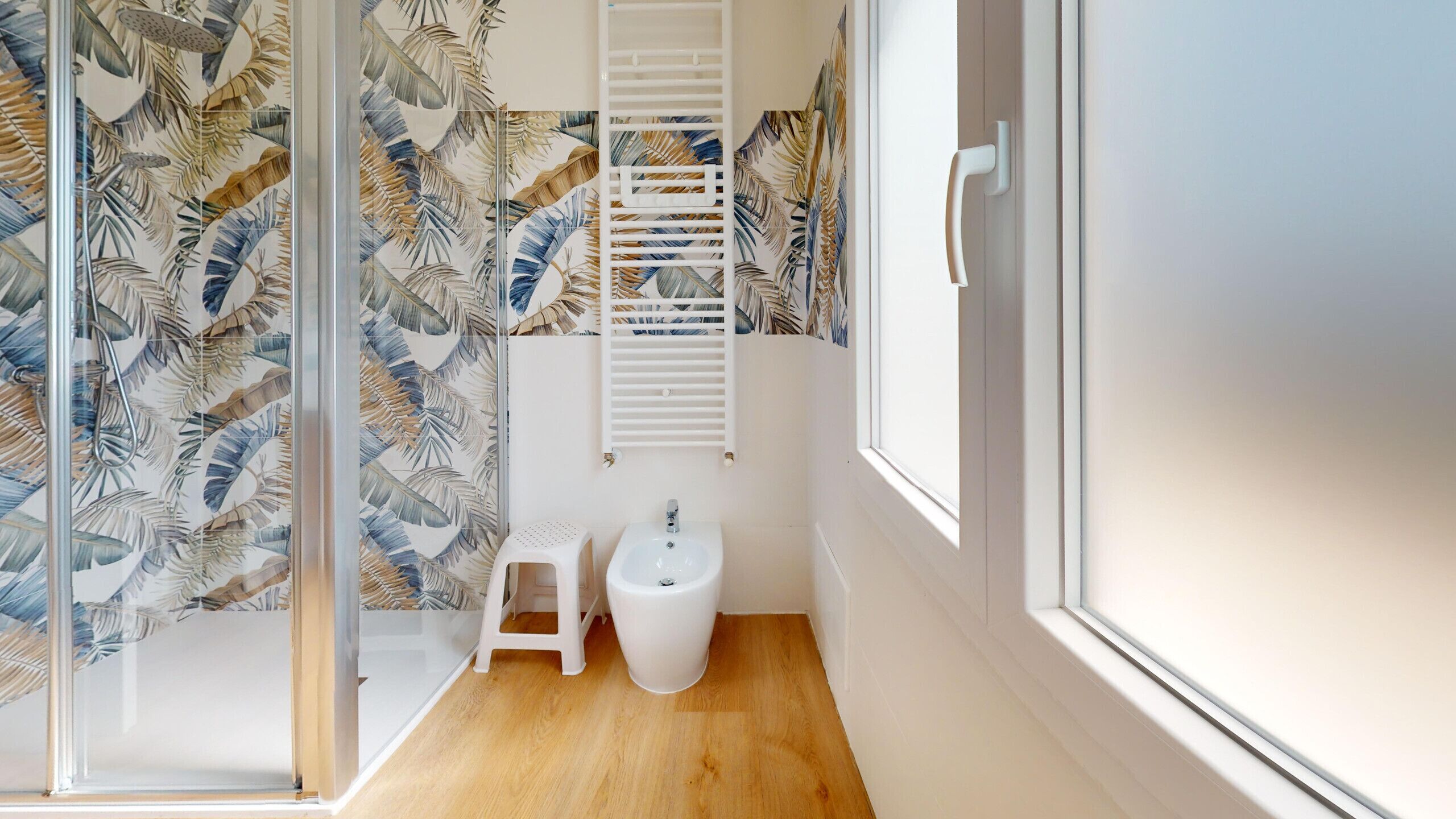 A bathroom with a shower, toilet, and sink, featuring a tropical leaf pattern on the walls.