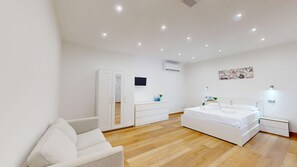 Un dormitorio con una cama, un armario blanco, un televisor y un cuadro en la pared.