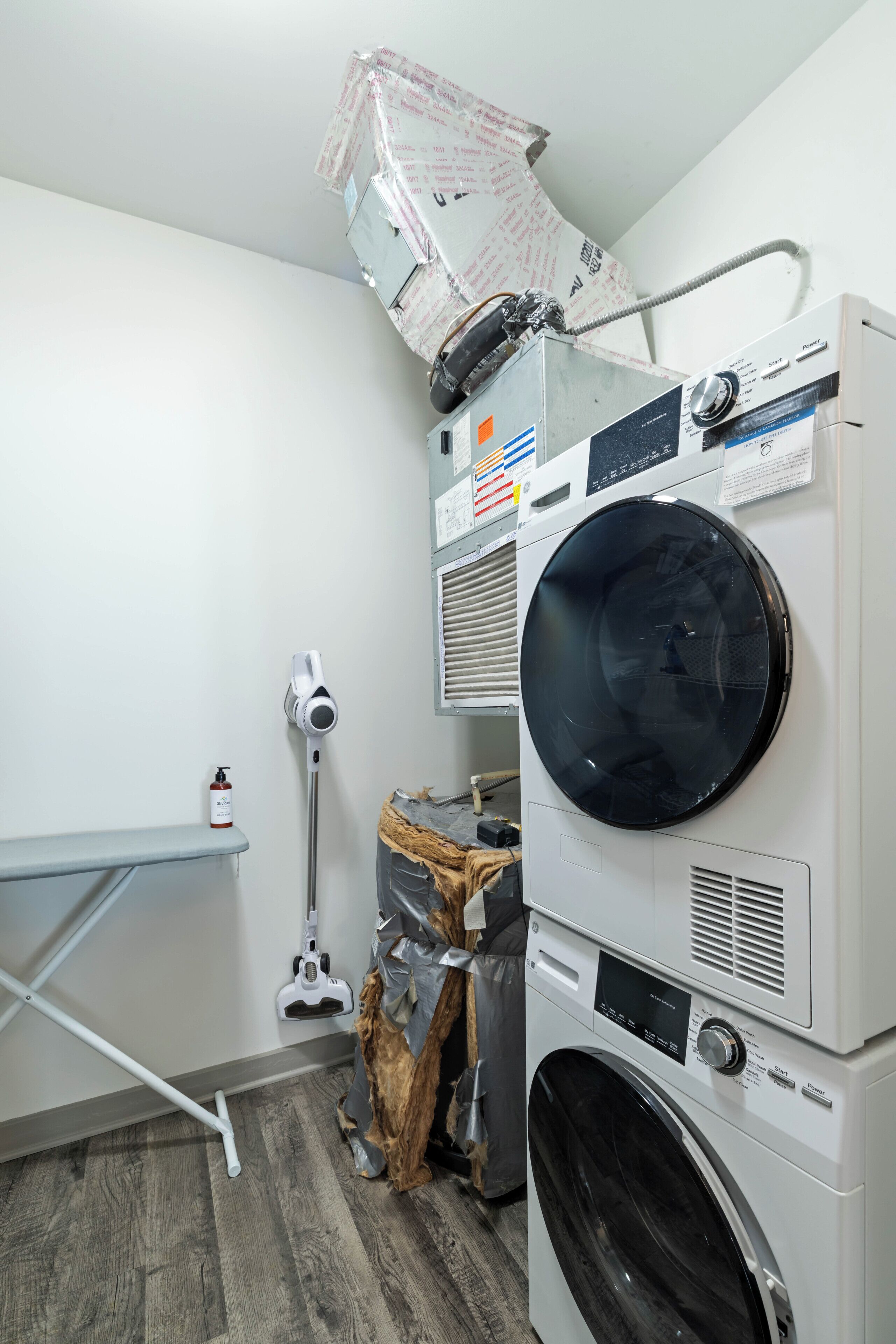 A laundry room with stacked washers and dryers, a mop, and a shelf.