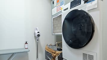 A laundry room with stacked washers and dryers, a mop, and a shelf.