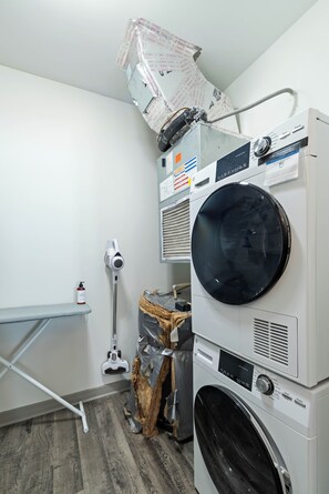 A laundry room with stacked washers and dryers, a mop, and a shelf.