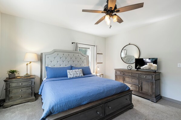 A bedroom with a bed, a ceiling fan, a dresser, a TV, and a lamp.