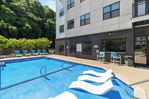 Una piscina con sillones de playa y un edificio con amplias ventanas.