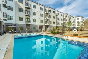 A modern apartment building with a swimming pool, outdoor seating, and a fenced garden area.