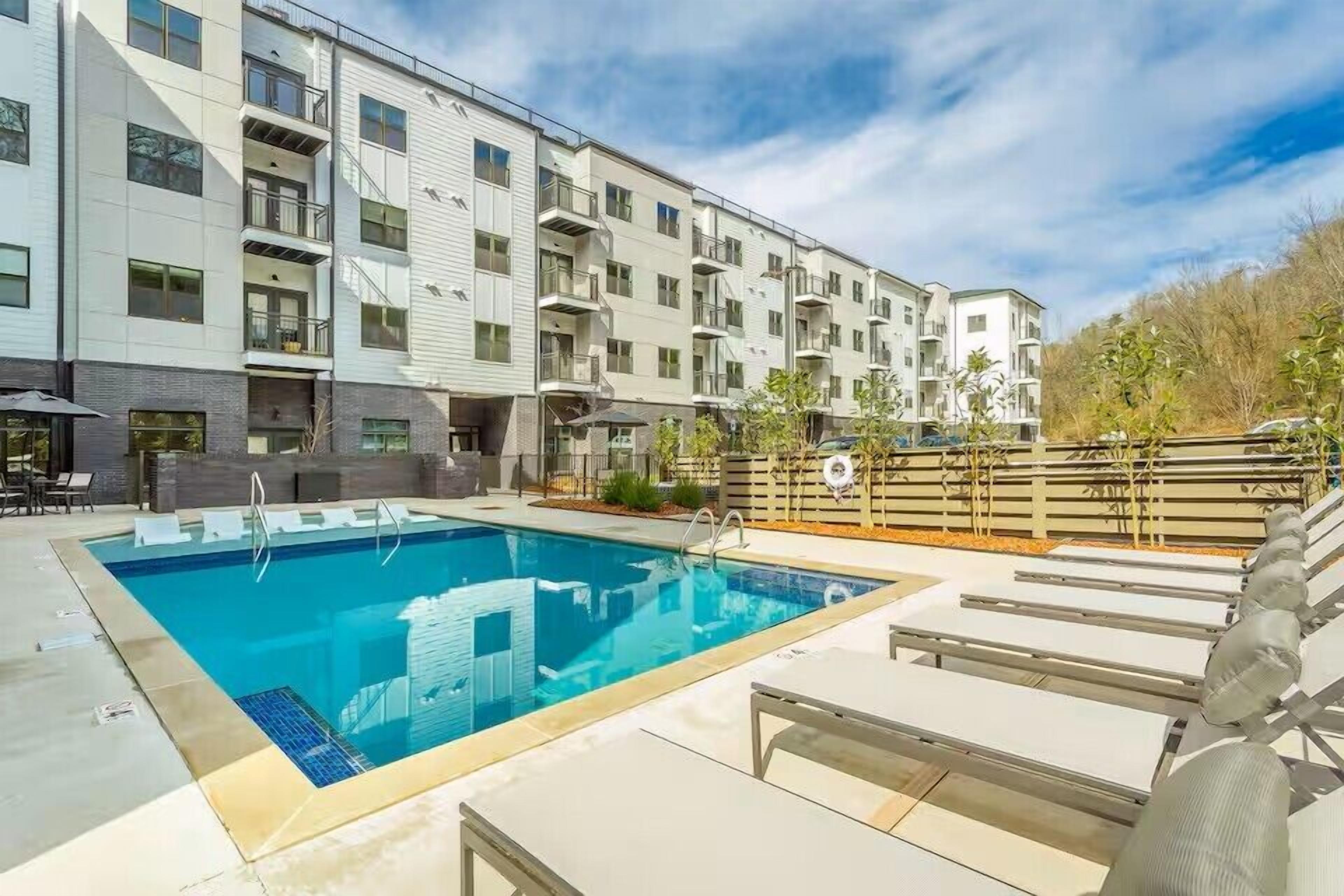 A swimming pool with lounge chairs and a multi-story building with balconies.
