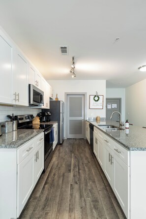 Una cocina moderna con armarios blancos, electrodomésticos de acero inoxidable y piso de madera.
