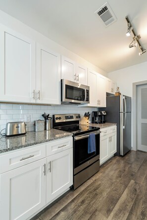 A modern kitchen with white cabinets, stainless steel appliances, and a granite countertop.
