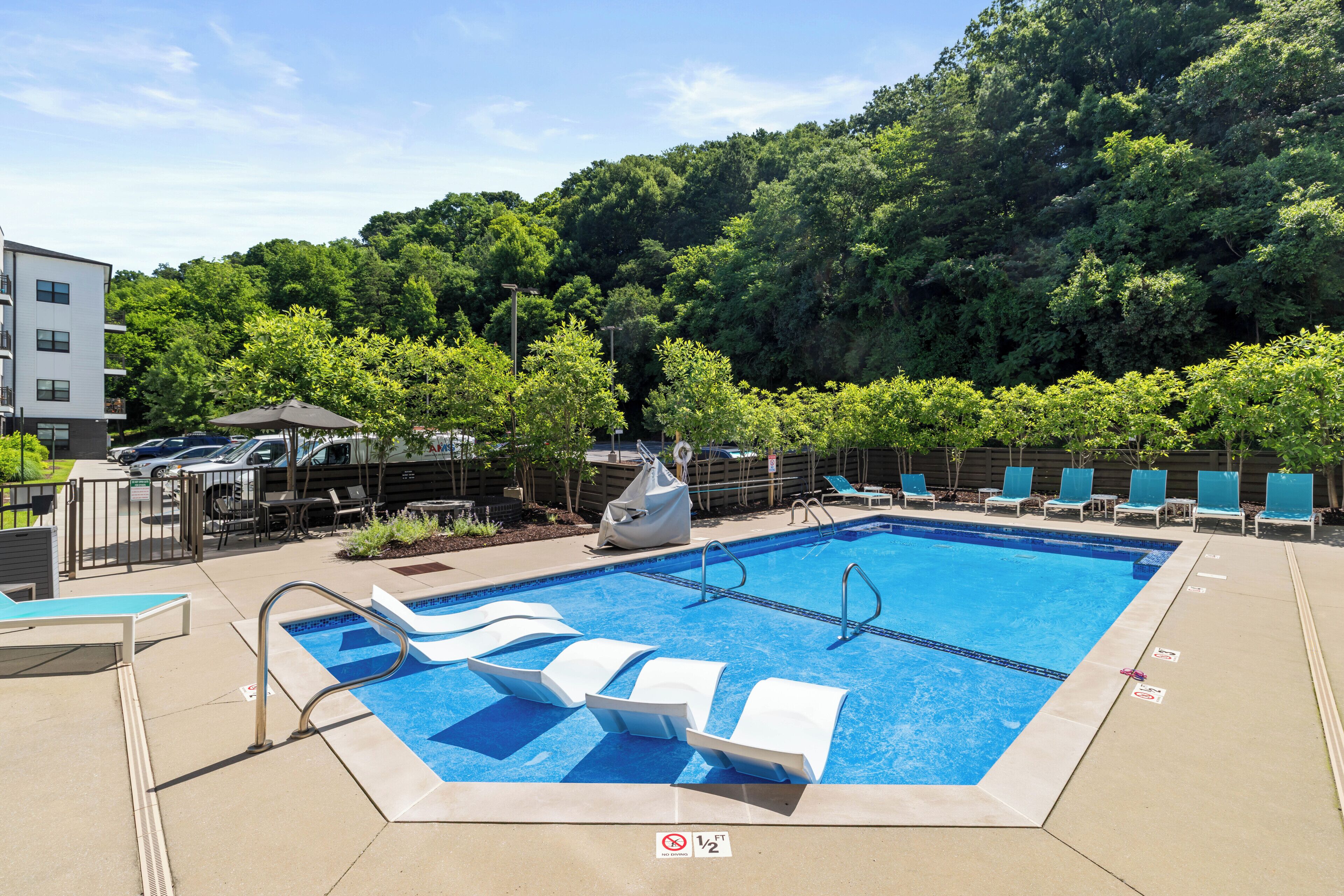 Piscina con sillas de descanso, zona de estar techada y vista a una ladera boscosa.