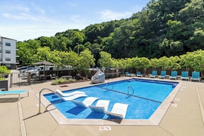 Una piscina amb gandules, una zona de seients coberta i vista a un vessant boscós.