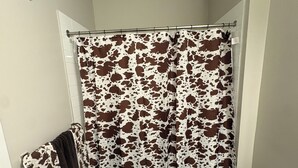 Un baño con cortina de ducha, inodoro, basurero y perchero para toallas.
