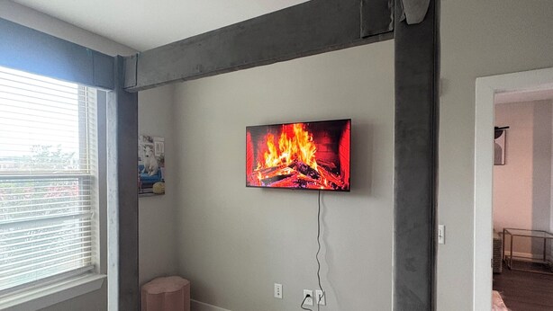 Un dormitorio con cama, ventilador de techo, televisor montado en la pared y ventana con persianas.
