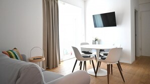 A modern living room with a sofa, a dining table with chairs, a TV mounted on the wall, and a large window with curtains. - SE295 - Senigallia, spacious three-room apartment with parking space and garden. (Senigallia)