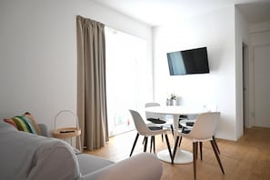 A modern living room with a sofa, a dining table with chairs, a TV mounted on the wall, and a large window with curtains. - SE295 - Senigallia, spacious three-room apartment with parking space and garden. (Senigallia)