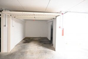A clean, empty hallway with white walls and a concrete floor, leading to a door with a red emergency exit sign. - SE295 - Senigallia, spacious three-room apartment with parking space and garden. (Senigallia)