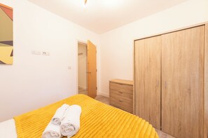 A bedroom with a bed, a wooden wardrobe, a wooden dresser, and a door leading to another room. - IBEX HOUSE (Reading)